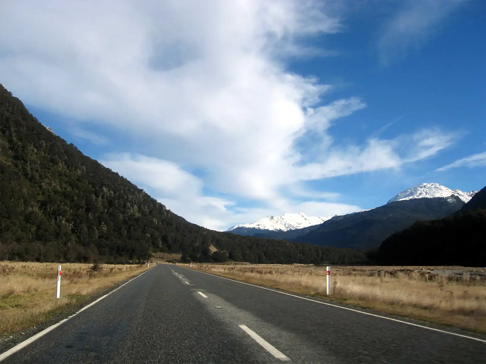 Route droite à travers une vallée d’herbes sèches vers des sommets enneigés, en direction de Wanaka