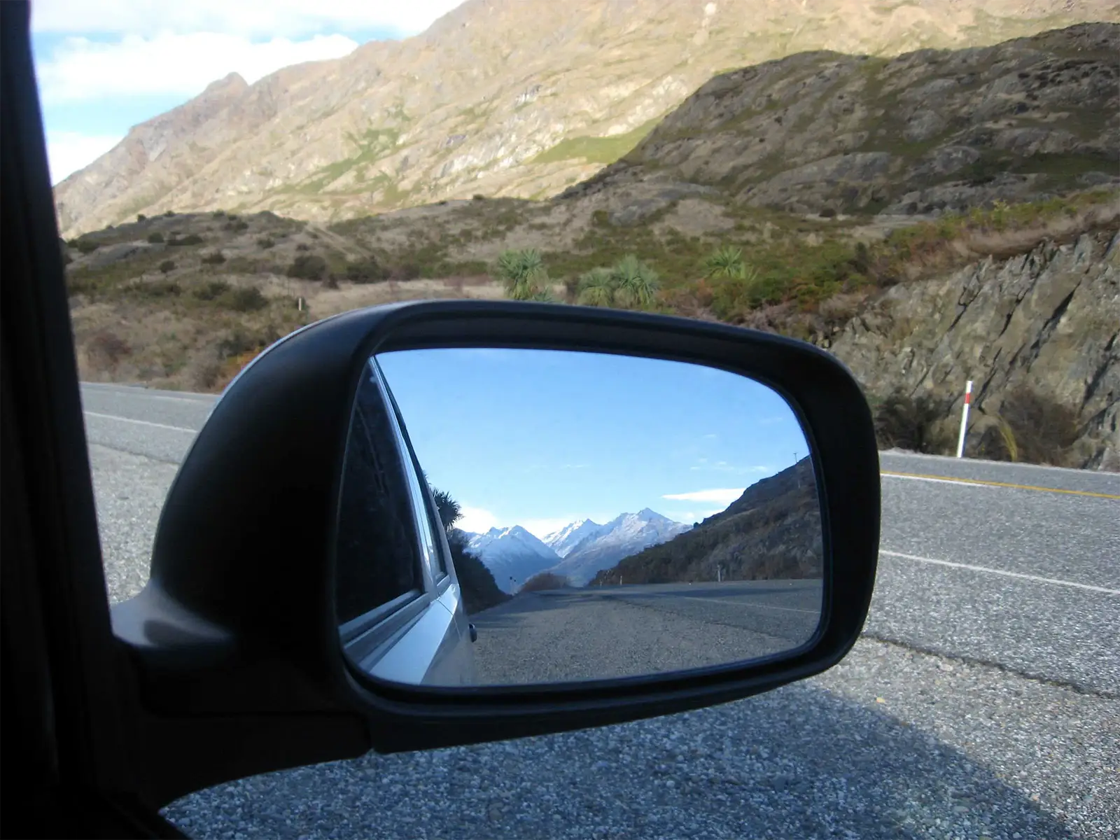 Sommets enneigés reflétés dans le rétroviseur de la voiture, sur une route de montagne vers Wanaka