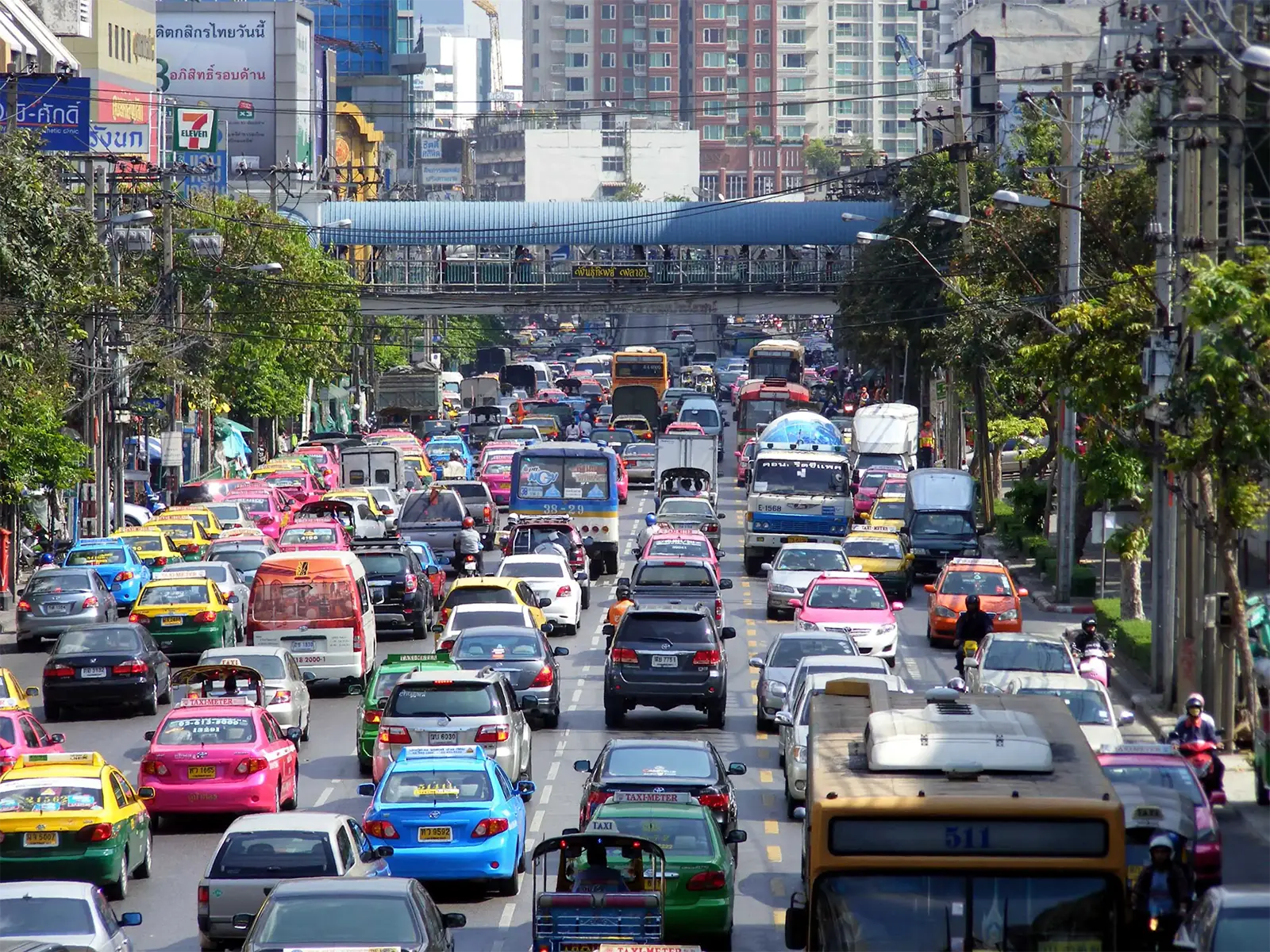 Avenue saturée de voitures, de bus et de taxis sous une passerelle piétonne à Bangkok