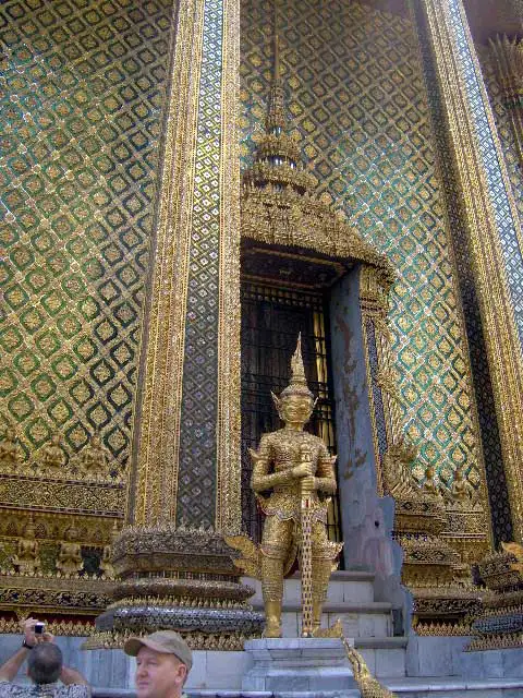 Statue de gardien dorée devant une porte couverte de mosaïques au Wat Phra Kaew à Bangkok