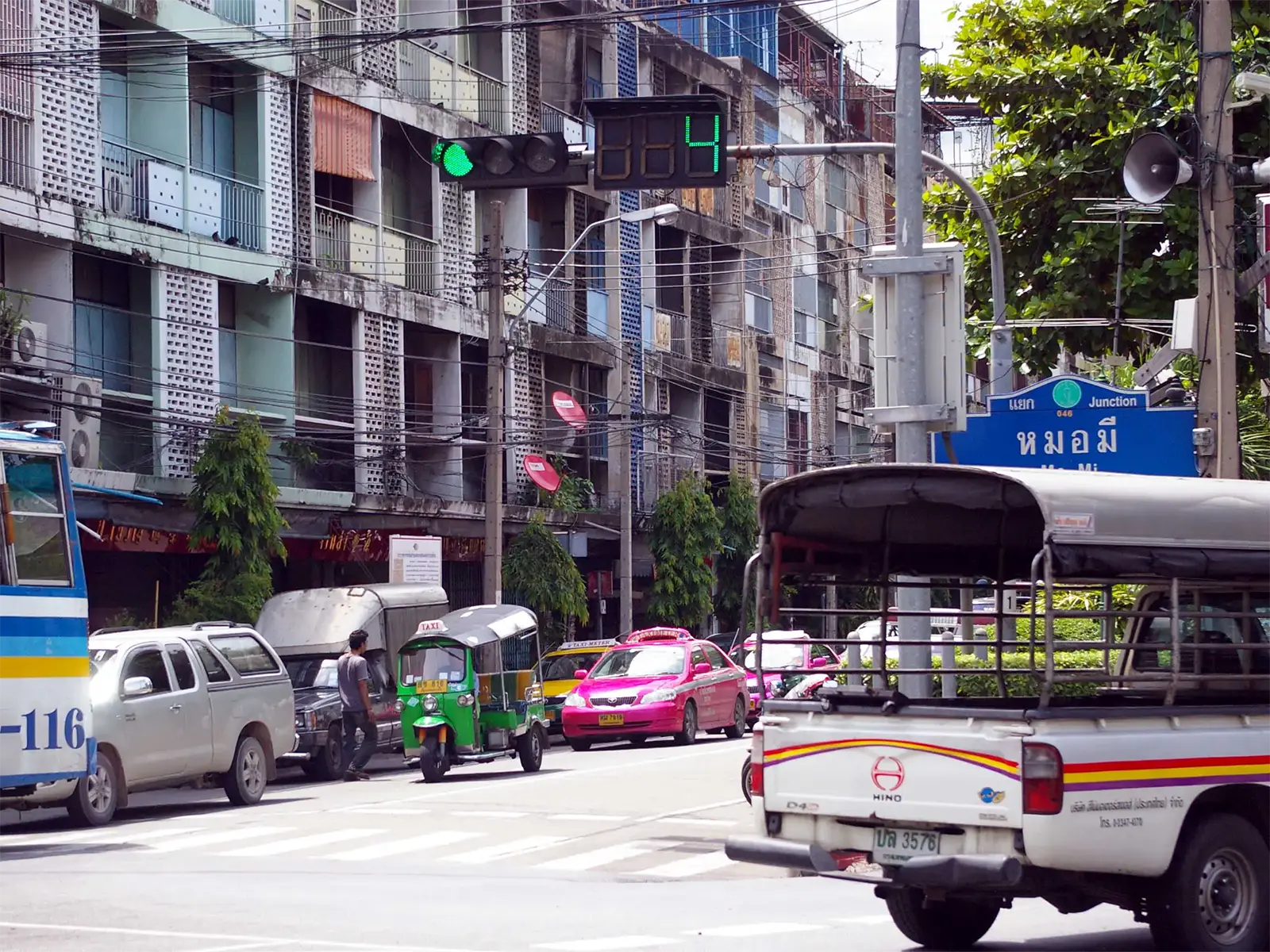 Tuk-tuk vert, taxi rose et songthaew à un carrefour animé de Bangkok