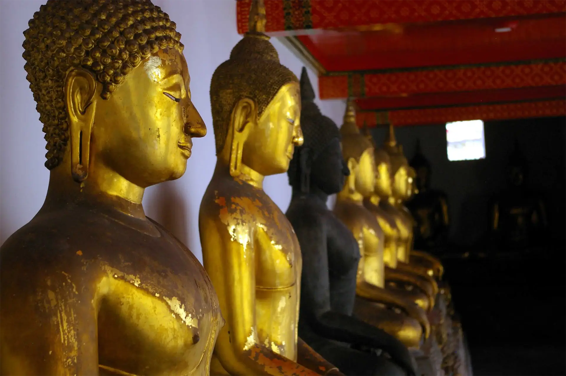 Rangée de bouddhas dorés et sombres dans la galerie couverte du Wat Pho à Bangkok