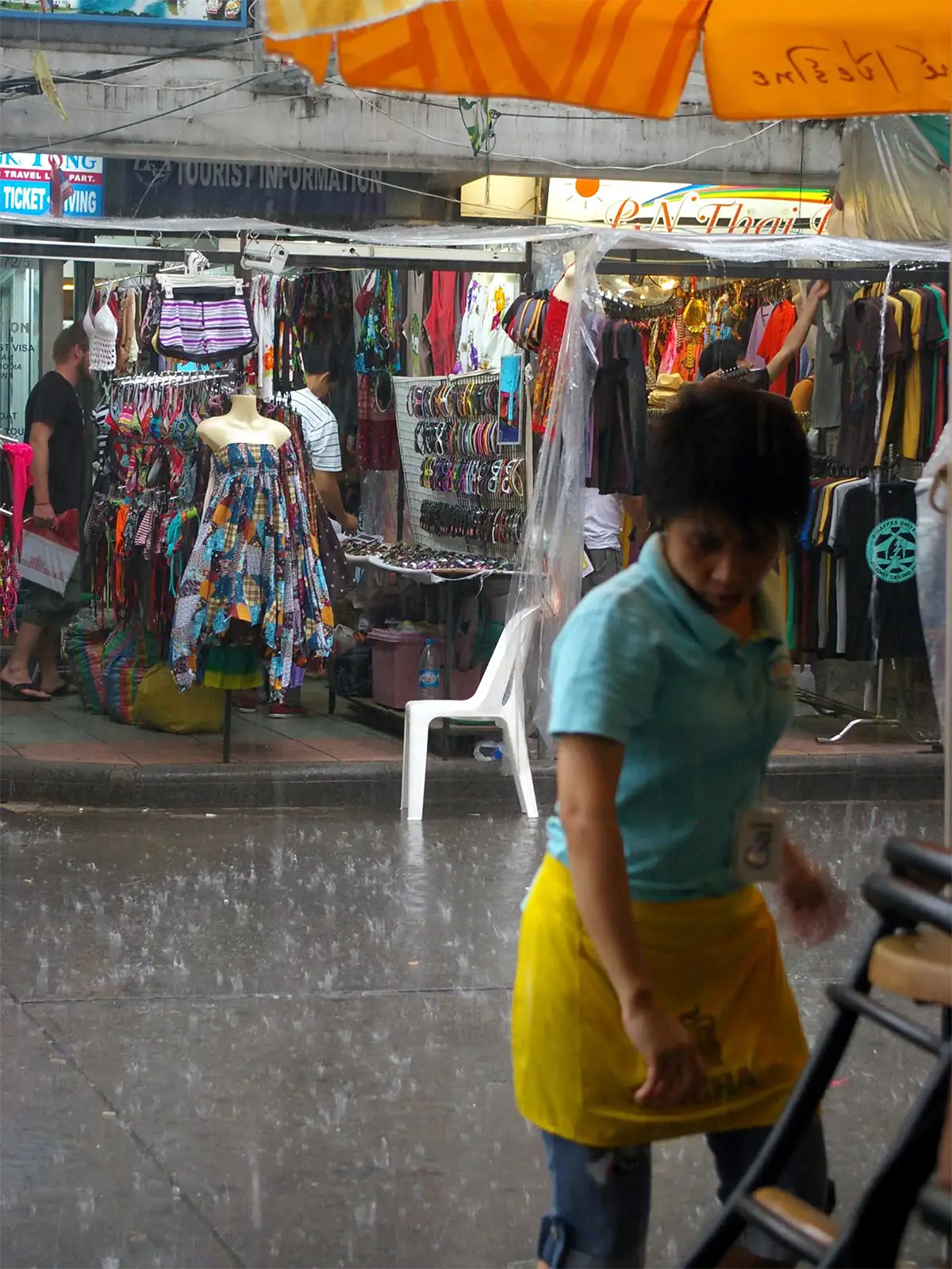 Averse tropicale sur une rue commerçante de Bangkok bordée d’étals de vêtements