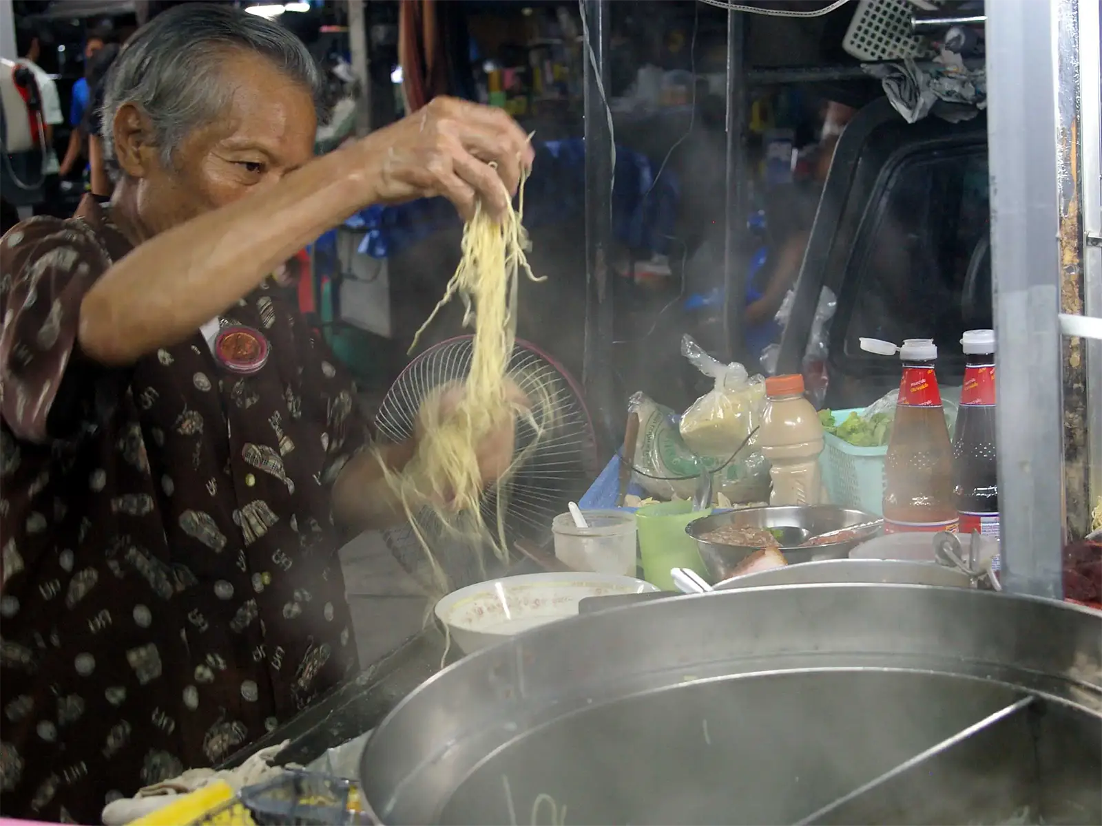 Vendeur âgé préparant des nouilles à son stand de cuisine de rue à Bangkok