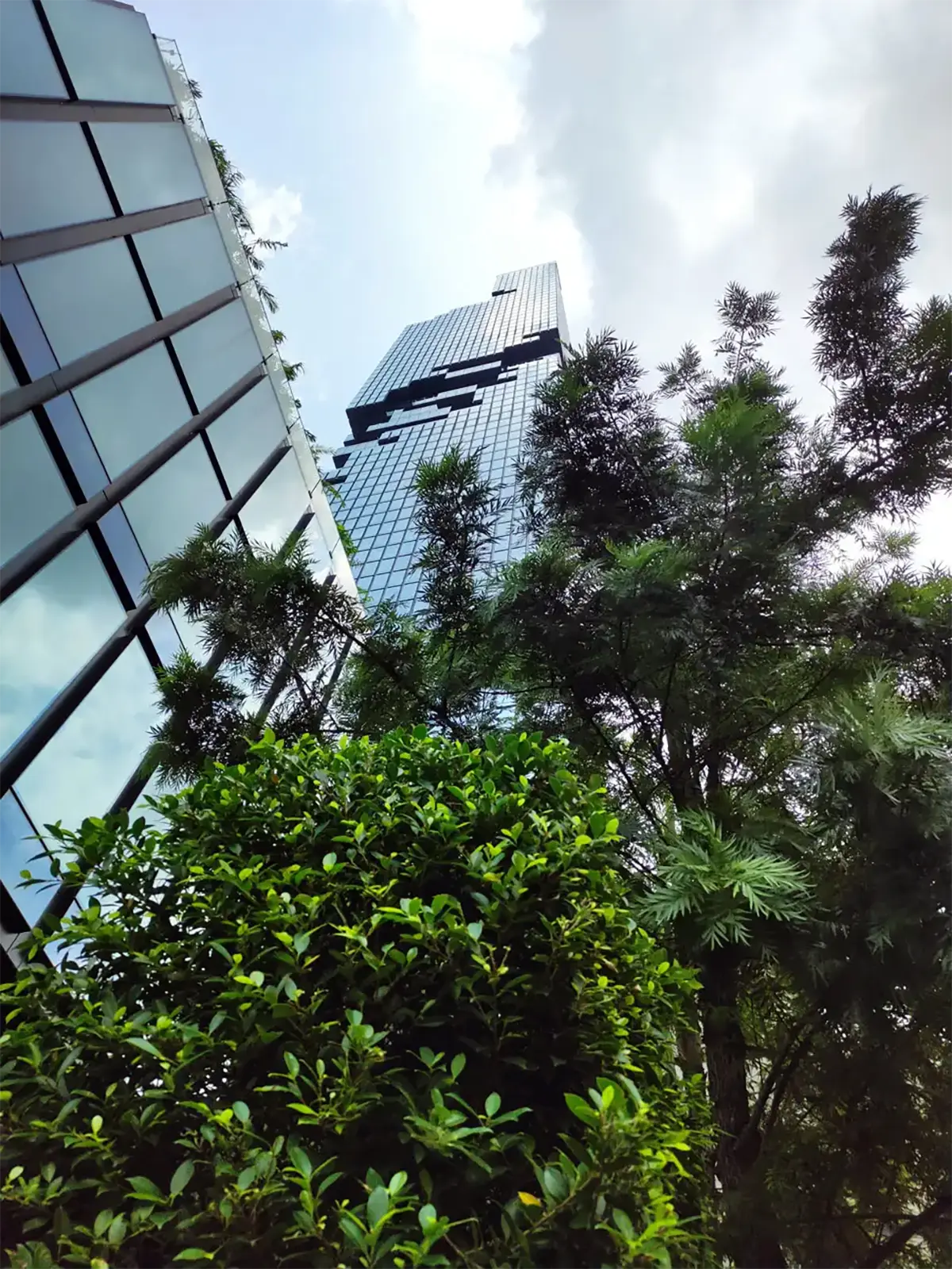 La tour MahaNakhon et sa façade pixellisée vue d’en bas à travers la végétation de Bangkok