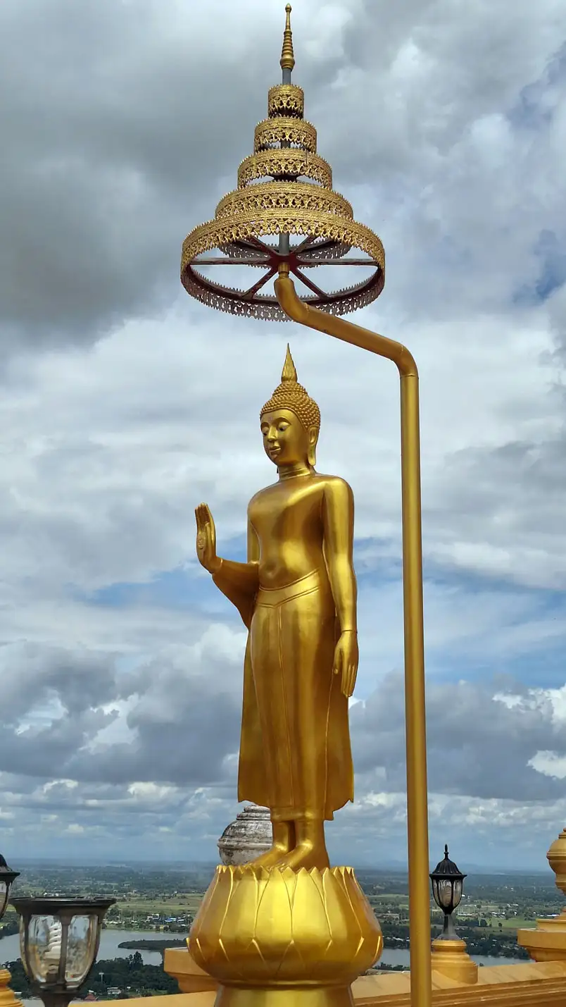 Bouddha debout doré sous une ombrelle ouvragée au sommet d’un temple de Nakhon Sawan