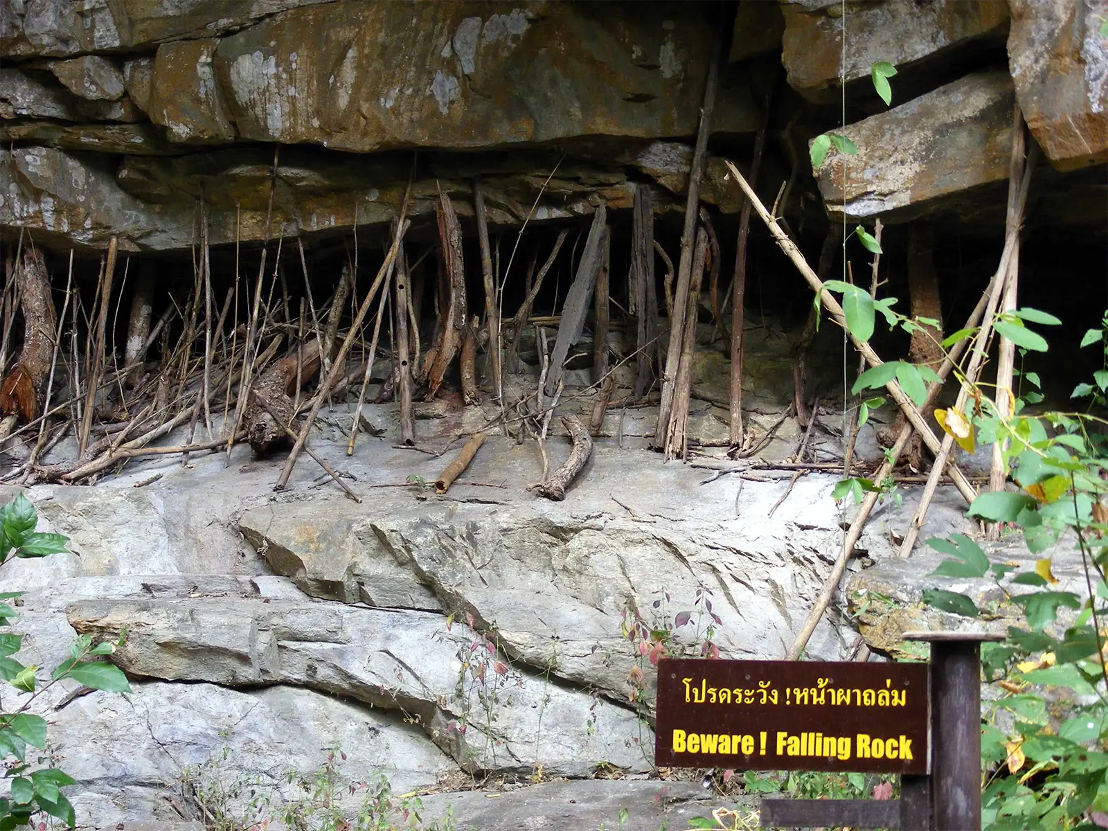 Bâtons de bois calés sous un surplomb rocheux près d’un panneau « Beware ! Falling Rock », nord de la Thaïlande