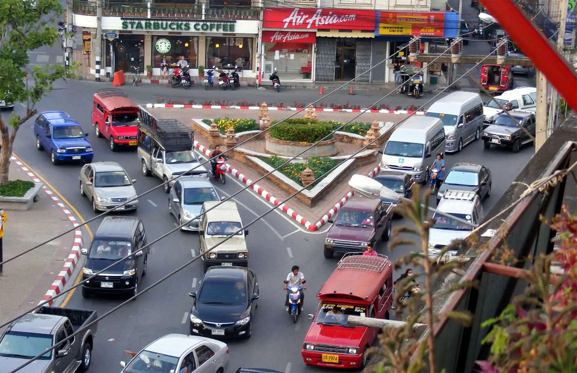Songthaews rouges et voitures autour d’un rond-point du centre de Chiang Mai