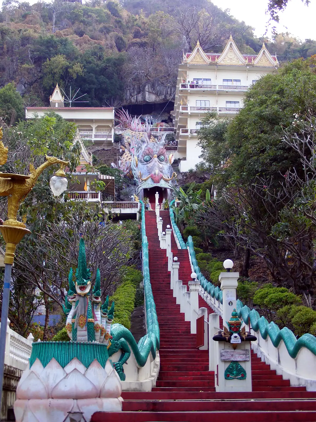 Escalier rouge bordé de nagas montant vers une grotte-temple en gueule de dragon près de Kanchanaburi