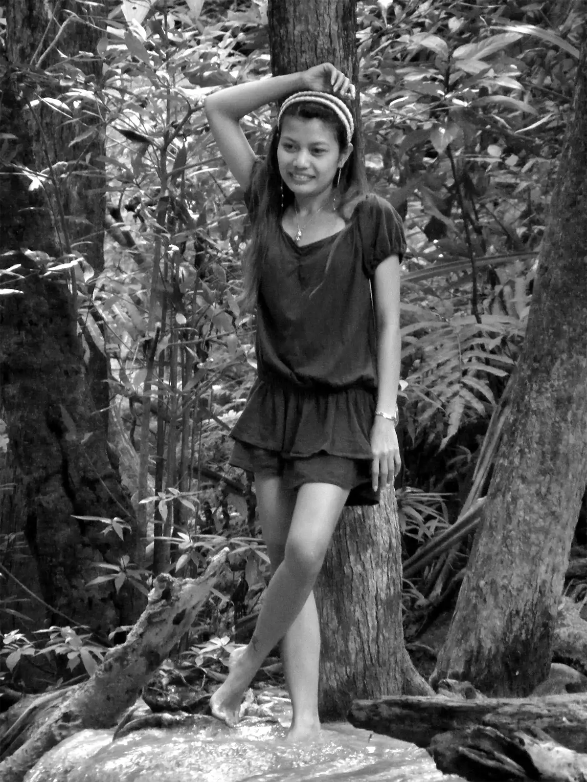 Jeune femme posant pieds nus contre un arbre dans la forêt près de Kanchanaburi, en noir et blanc