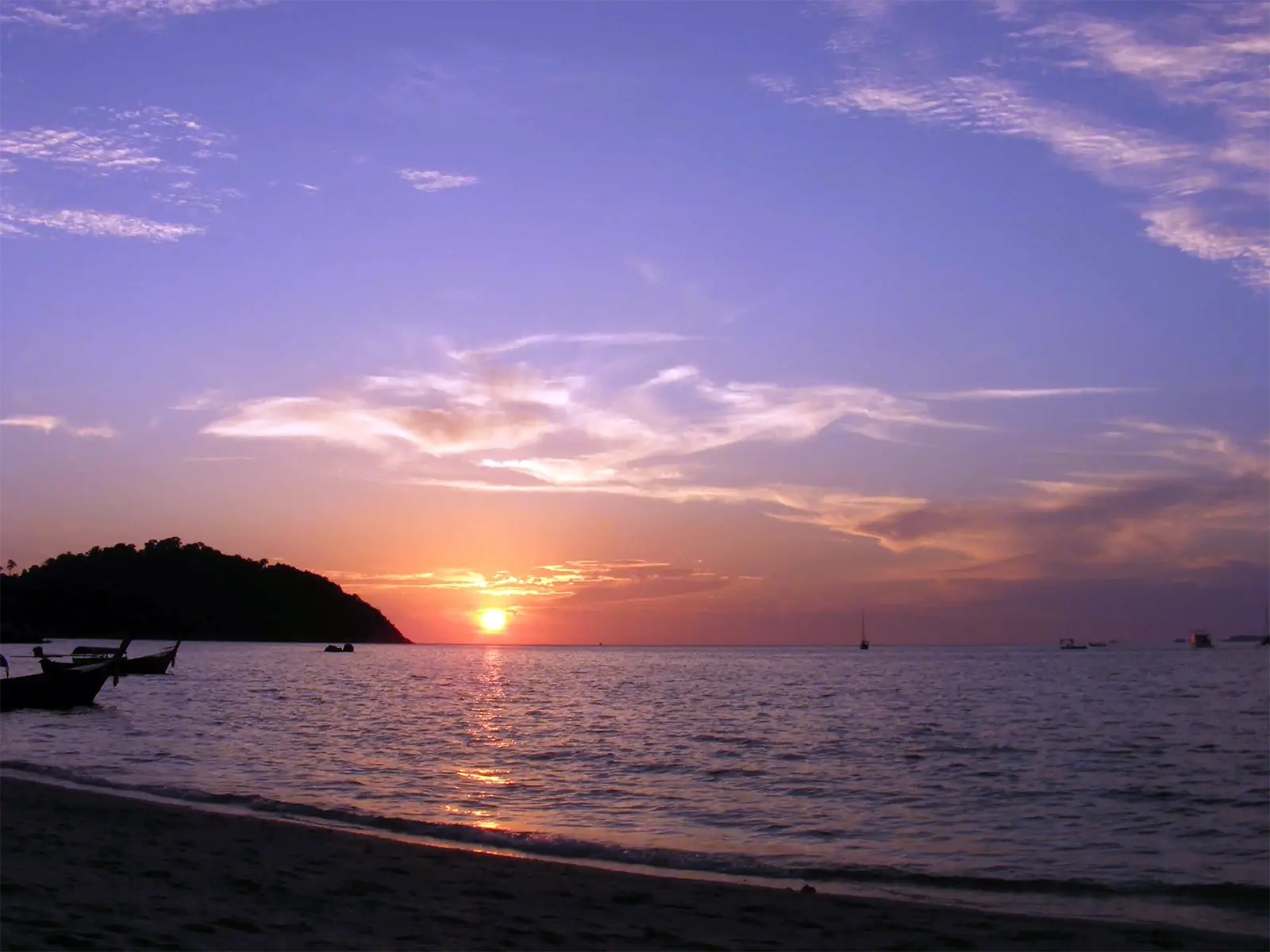 Coucher de soleil sous un ciel violet, avec bateaux à longue queue au bord d’une plage de Koh Lipe