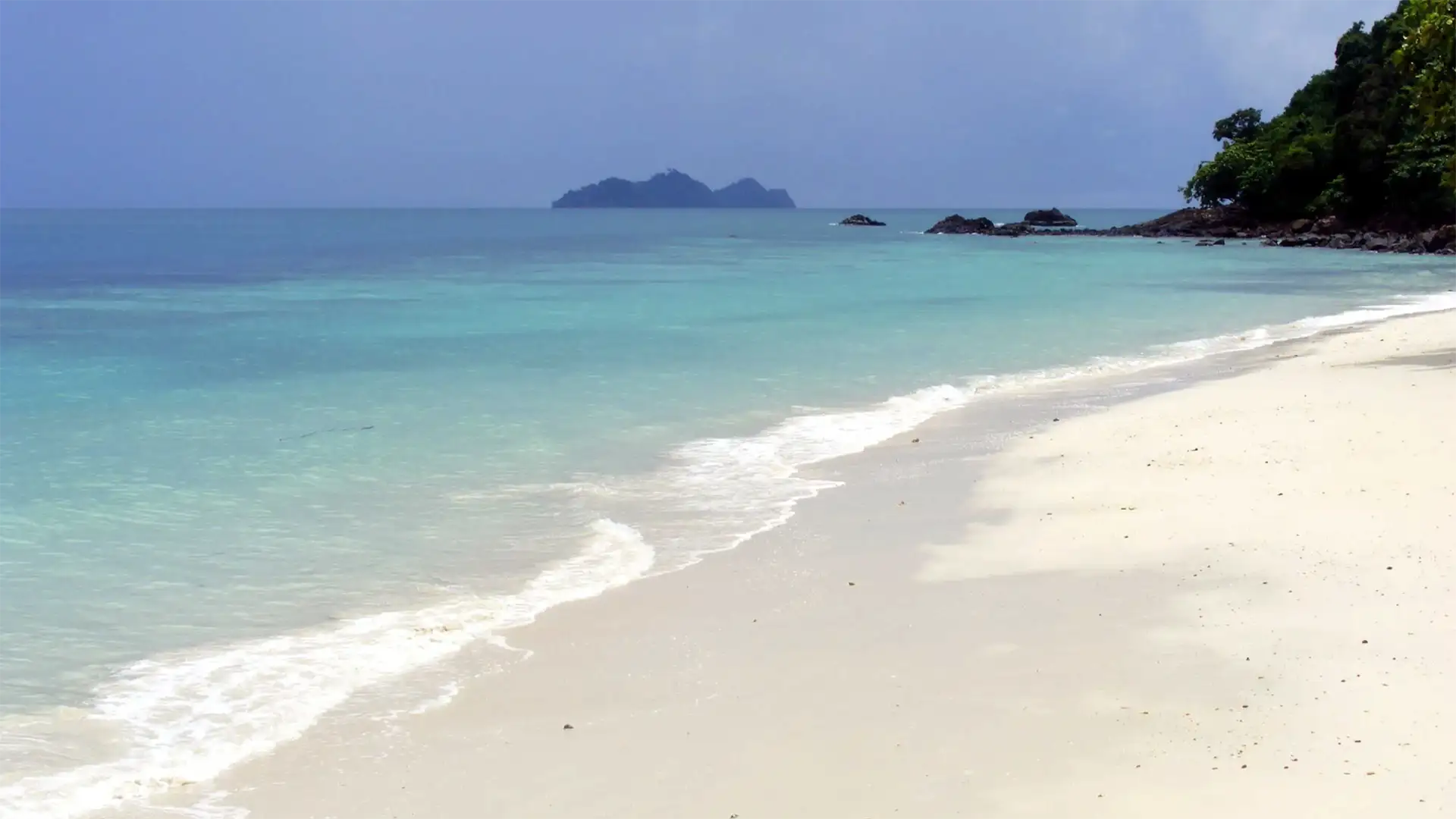 Plage de sable blanc déserte et mer turquoise sous un ciel d’orage à Koh Ngai