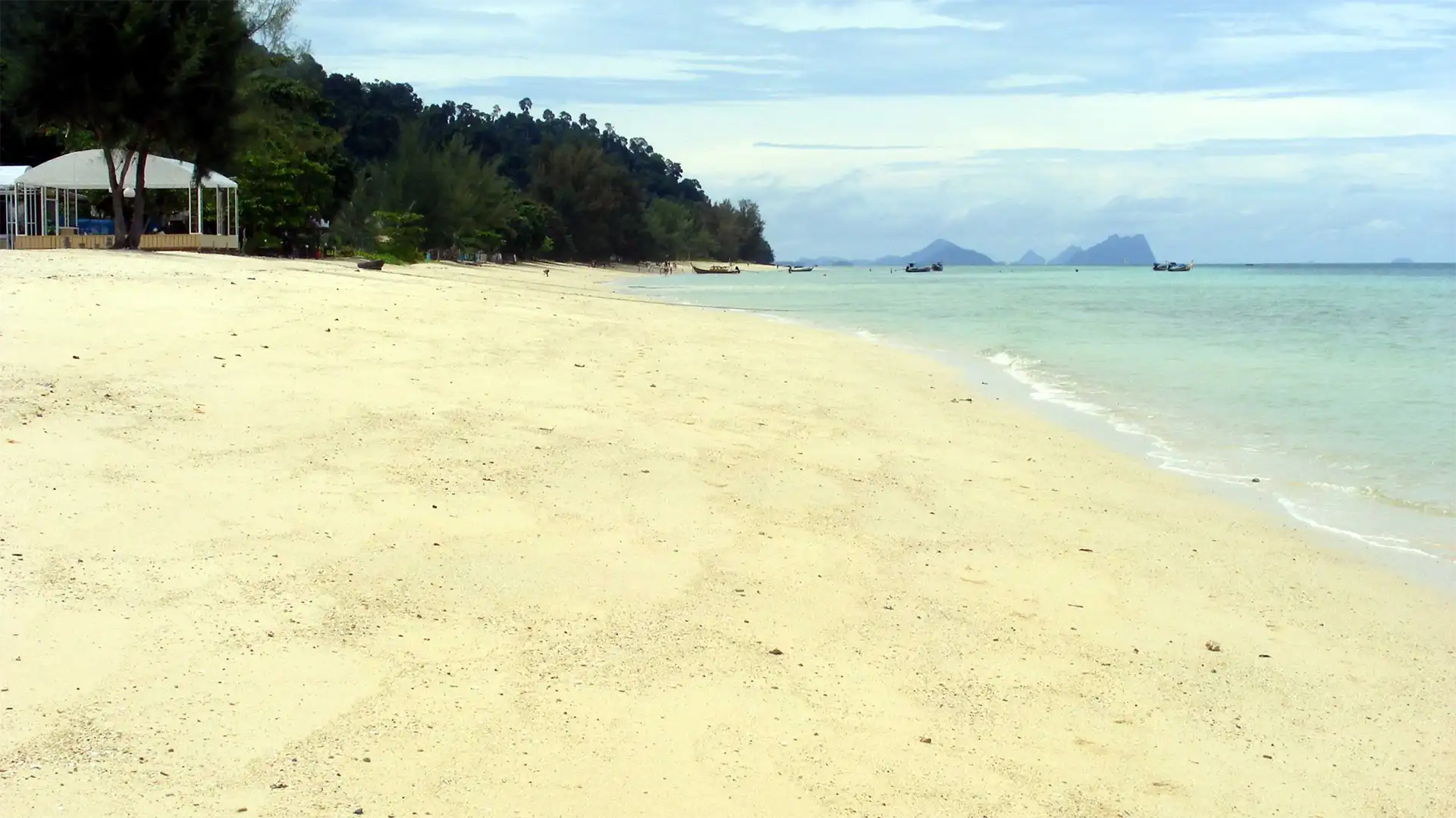 Longue plage de sable blanc presque déserte avec une paillote à l’ombre des arbres à Koh Ngai