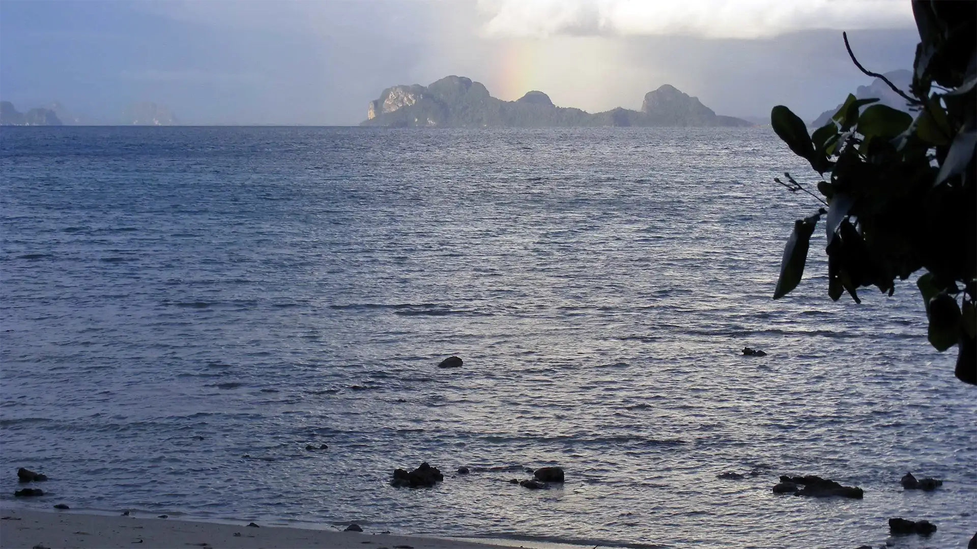 Arc-en-ciel au-dessus des îlots calcaires sous un ciel d’orage, vu depuis Koh Ngai
