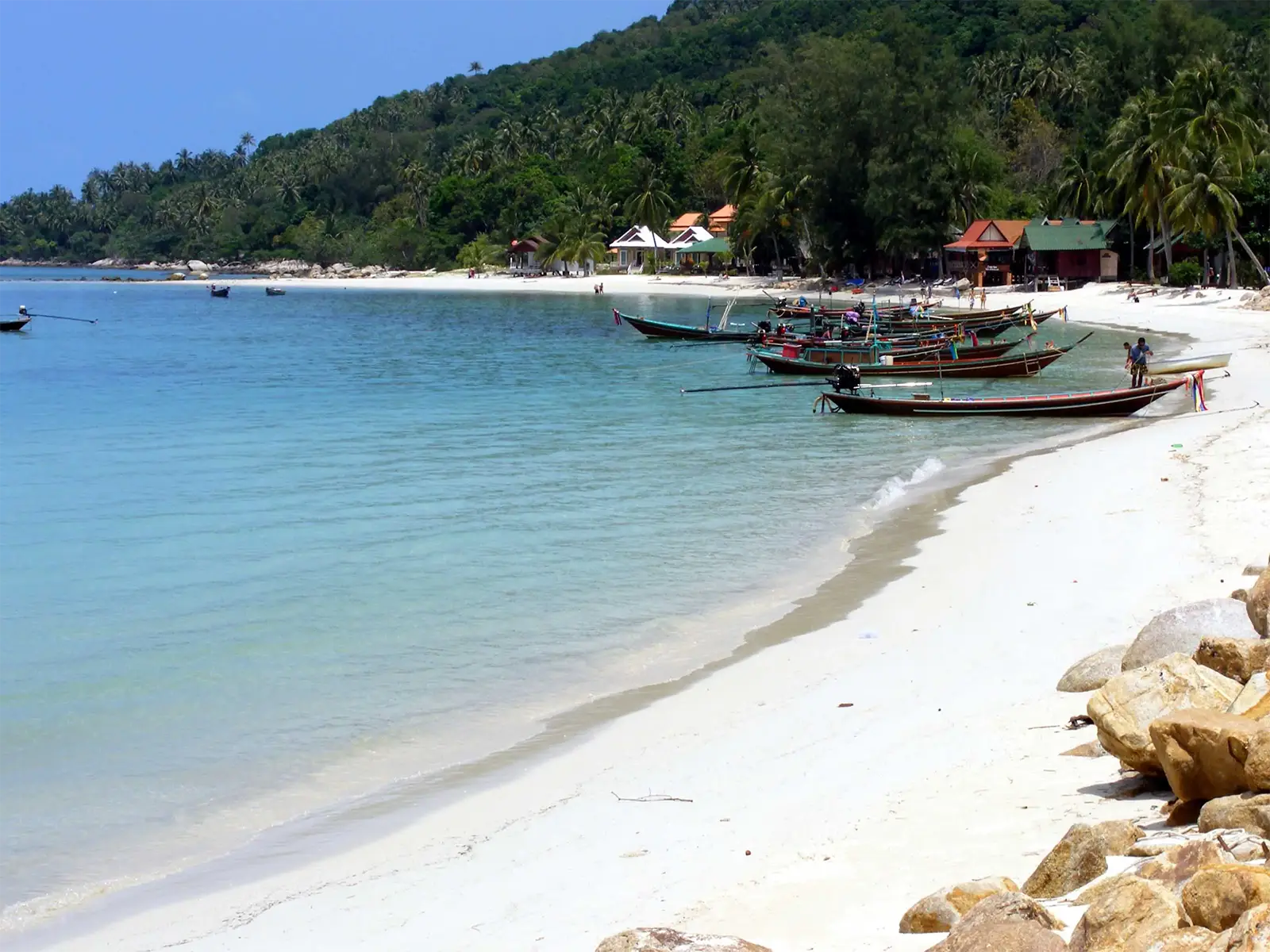 Plage de sable blanc, rochers et bateaux à longue queue au pied des collines de Koh Phangan