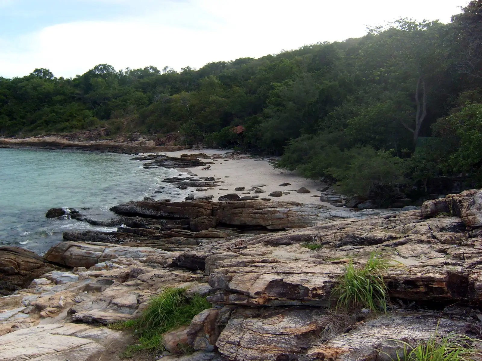 Crique de sable blanc entre rochers plats et forêt, sur une île de l’est de la Thaïlande