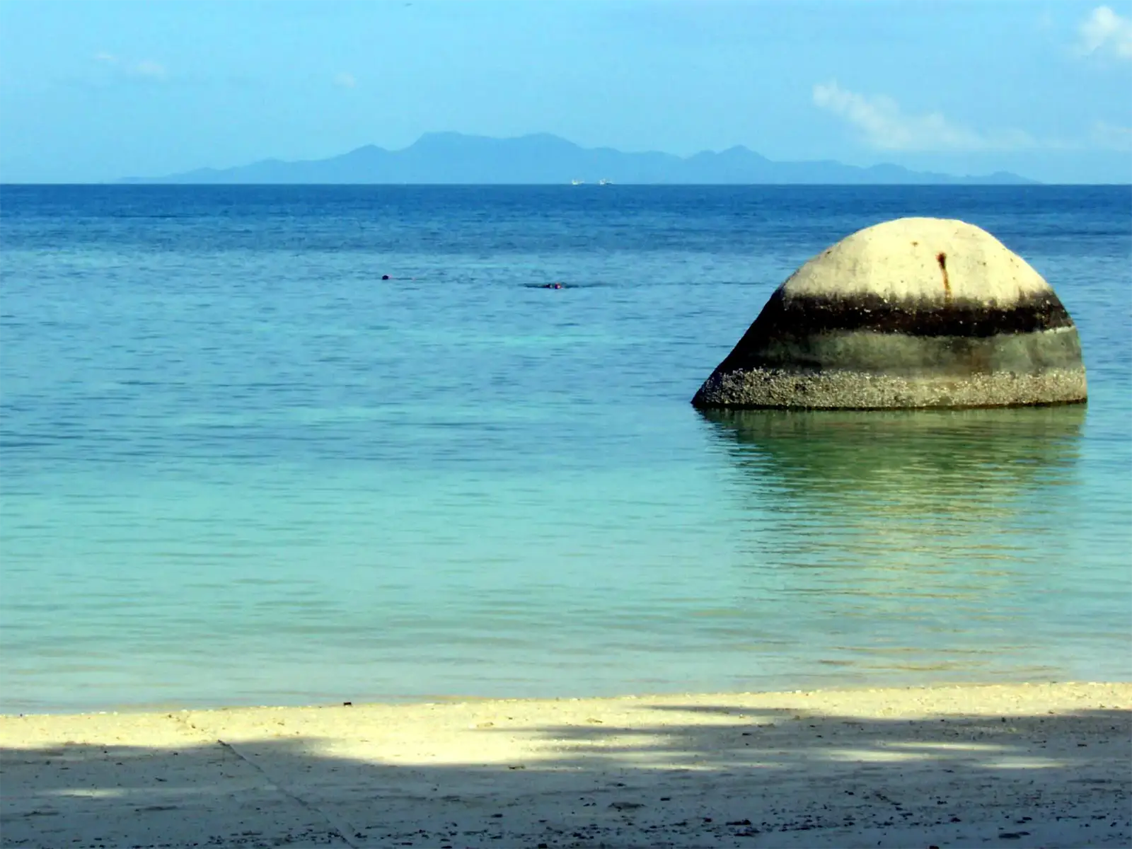 Rocher arrondi dans une eau turquoise limpide, île montagneuse à l’horizon depuis Koh Tao