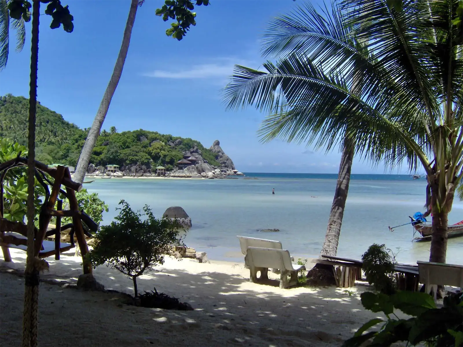 Bancs à l’ombre des palmiers face à une baie et son promontoire rocheux à Koh Tao