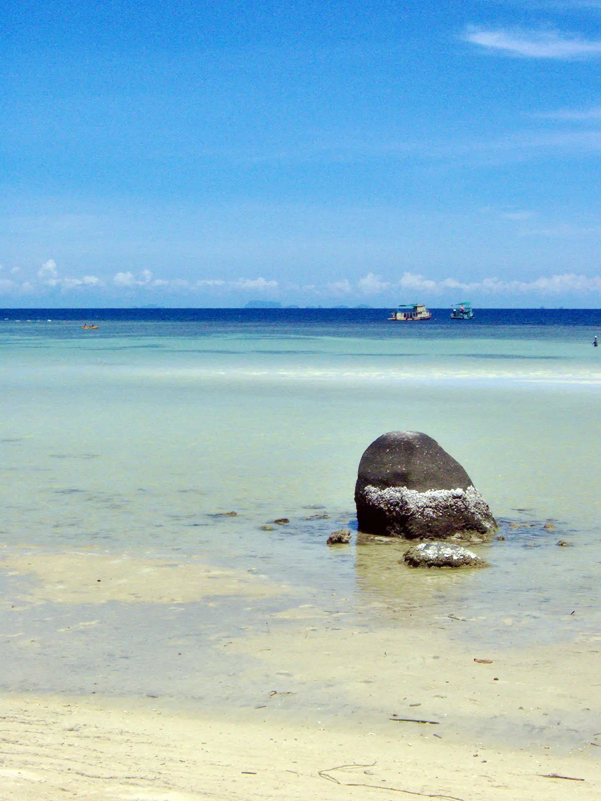 Rocher sombre dans l’eau claire et peu profonde, bateaux de plongée au large de Koh Tao