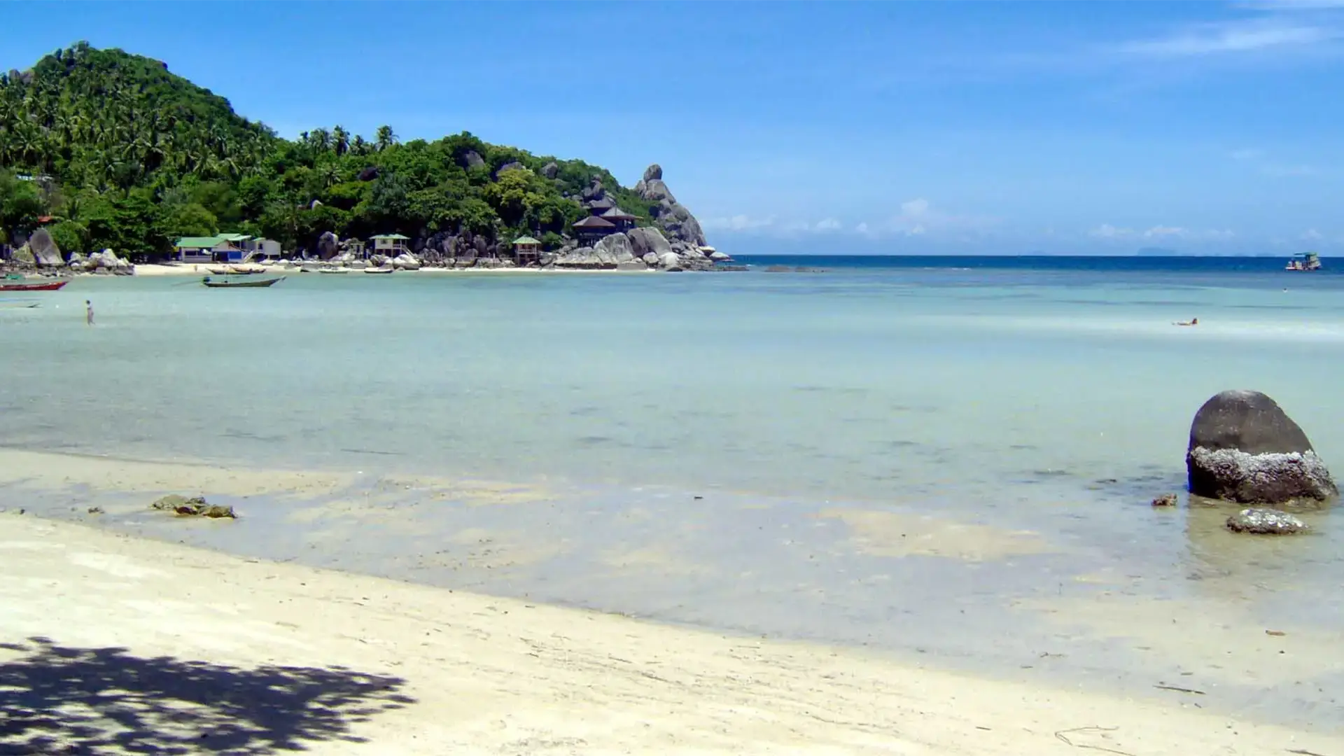 Plage de sable blanc, eau limpide et promontoire rocheux couvert de jungle à Koh Tao