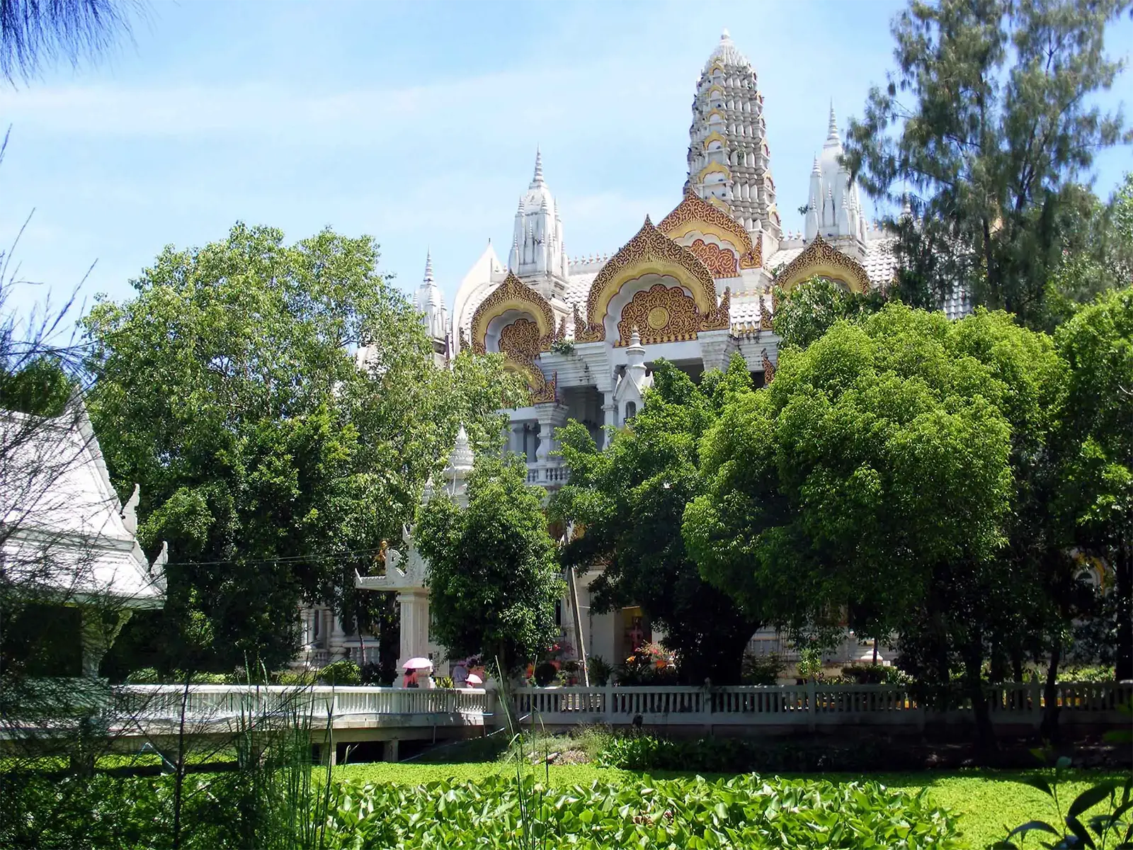 Le temple blanc et doré du Wat Phai Rong Wua derrière les arbres à Suphan Buri