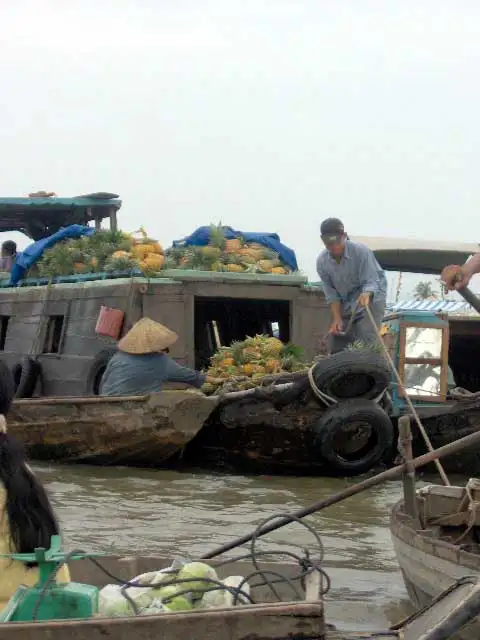 Bateaux chargés d’ananas et vendeuse au chapeau conique sur un marché flottant du Mékong