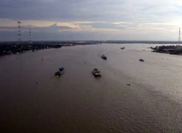 Bateaux sur un large bras du Mékong au crépuscule, vus du haut d’un pont dans le delta