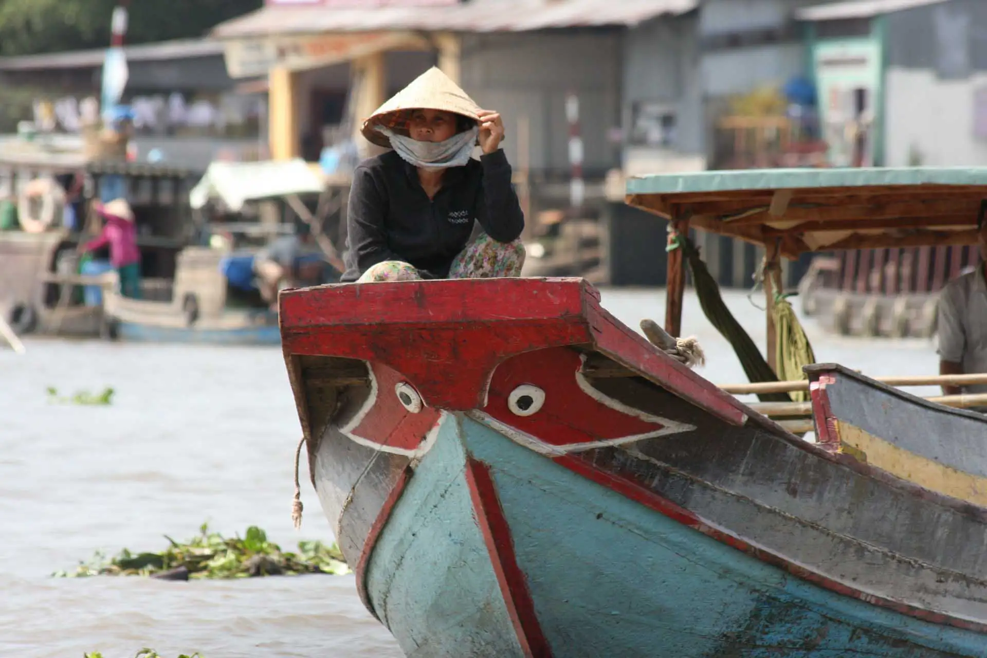 Femme au chapeau conique assise à la proue peinte d’une barque, dans le delta du Mékong