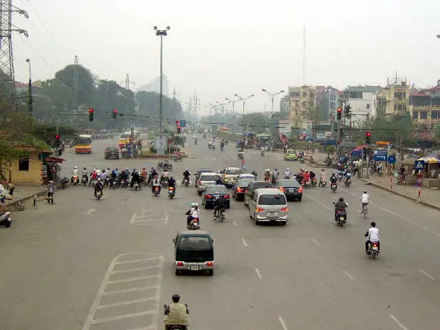 Large avenue encombrée de scooters et de voitures à l’entrée de Hanoï