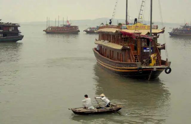 Jonque touristique en bois et barque à rames dans la brume de la baie d’Halong