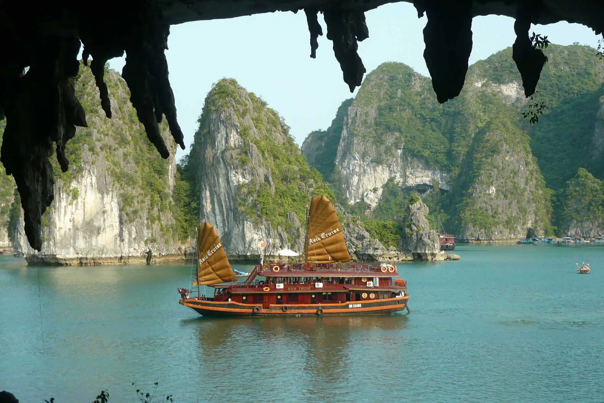 Jonque aux voiles ocre entre les pitons karstiques, vue depuis une grotte de la baie d’Halong