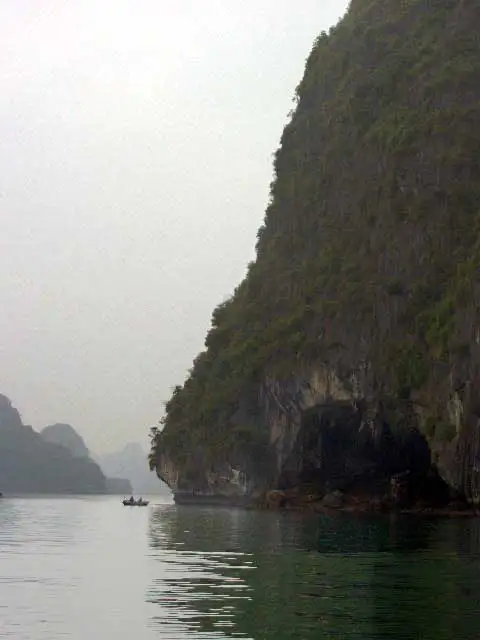 Barque minuscule au pied d’une falaise karstique, dans la brume de la baie d’Halong