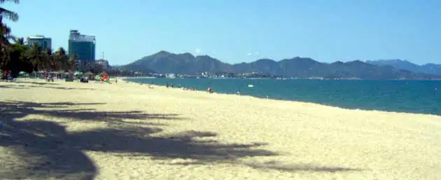 La longue plage de sable de Nha Trang, ses palmiers et ses montagnes au loin