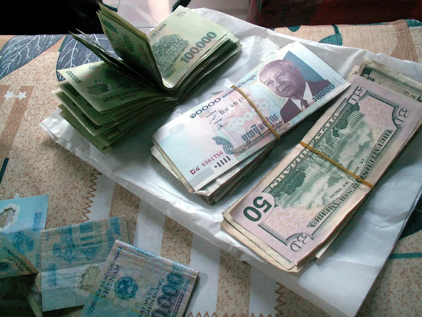 Liasses de dongs, de riels cambodgiens et de dollars posées sur un lit à Saïgon