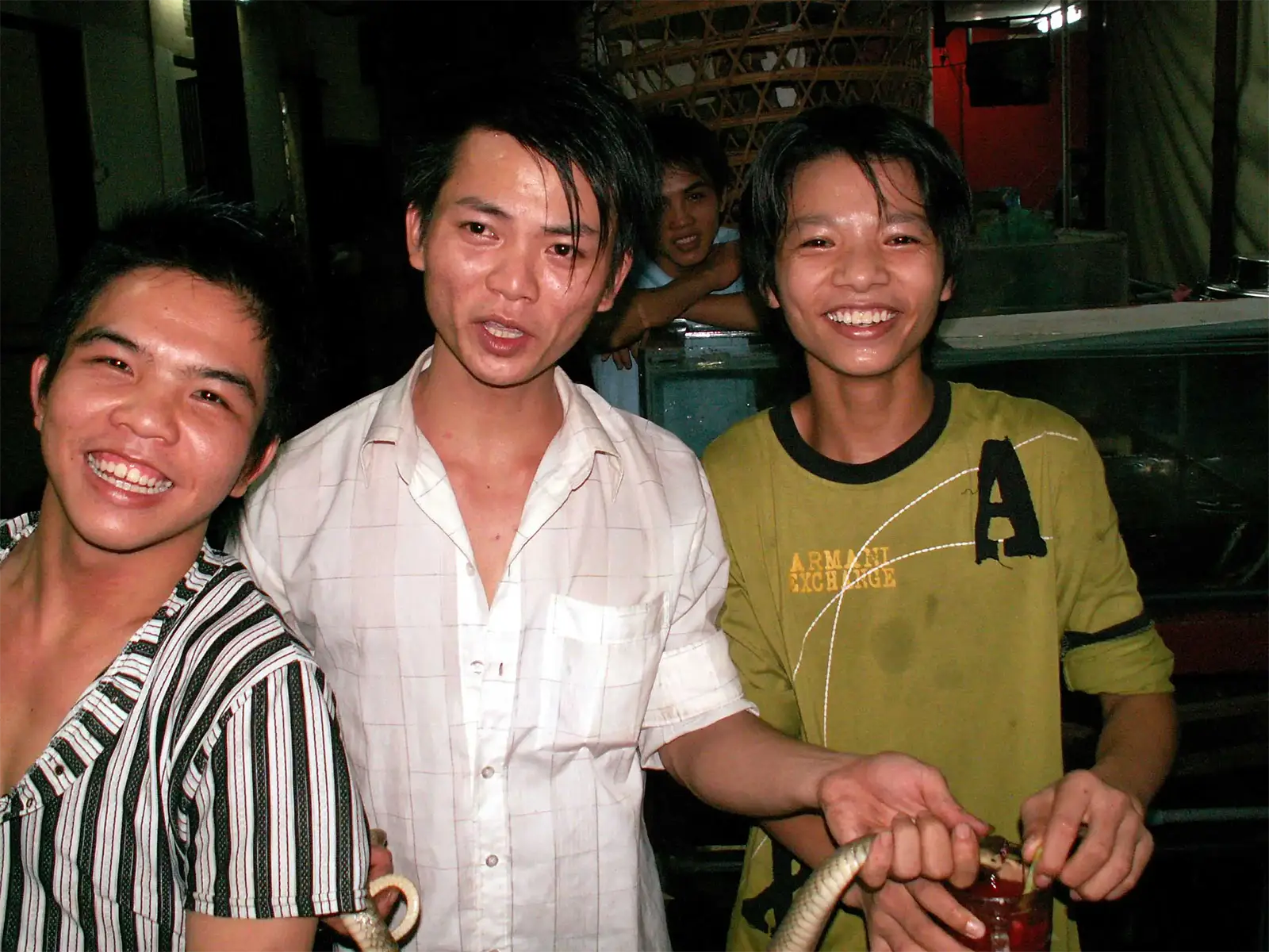 Jeunes Vietnamiens souriants tenant le cobra et un verre de son sang, à Saïgon